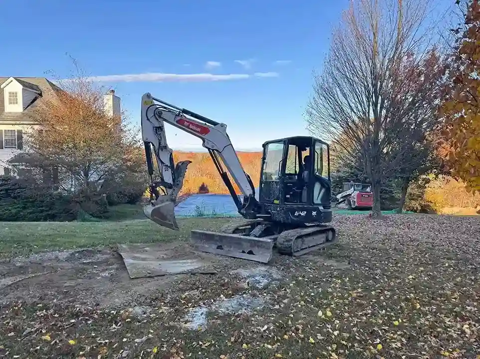 A small excavator parked beside a house, ready for excavation work on the property.