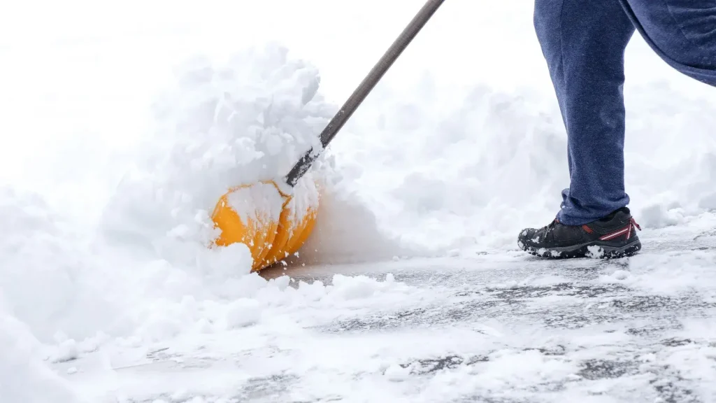 A person shoveling snow with a yellow shovel, demonstrating effective snow and ice management techniques.