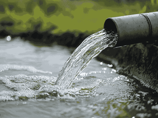 A drainage pipe is discharging water into a stream, illustrating the flow of water from one environment to another. 